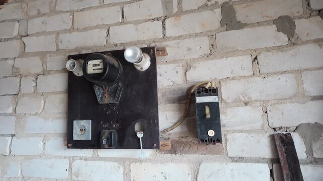 Obsolete electrical equipment, including a meter, fuses, and switches, mounted on a rustic white brick wall in an old building, capturing a sense of decay and vintage technology