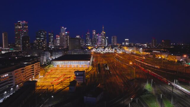 Aerial view of the Hauptbahnhof central station with glowing tracks and the city skyline under a dark blue twilight sky in Frankfurt am Main, Hessen, Germany.