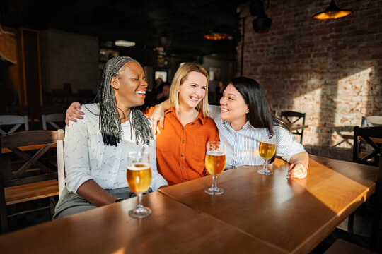 Three diverse women friends enjoying beer and laughing in a pub