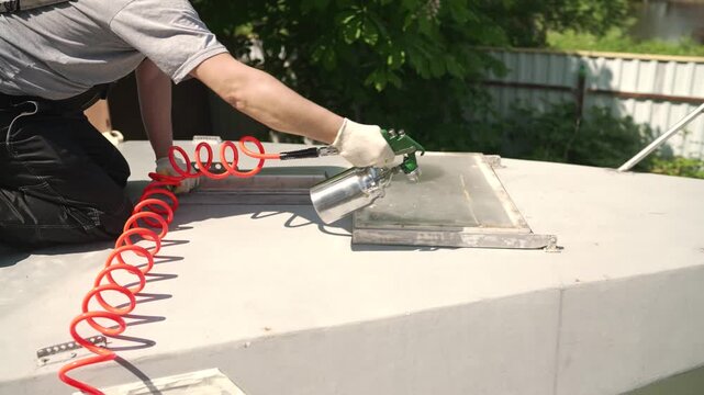 A worker in overalls uses an air spray gun to paint a metal hatch on a boat deck. Close up shot of professional painting and restoration work outdoors. DIY boat maintenance and repair
