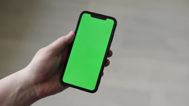 Hand holding a smartphone with a green screen for easy editing and customization