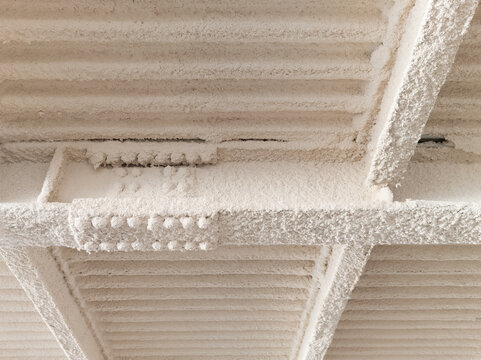 Close-up photograph of spray-applied fireproofing insulation on industrial steel beams and corrugated metal ceiling decking