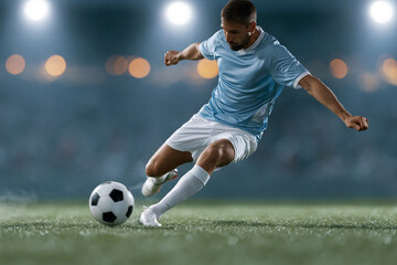 Naklejka premium Player dribbles ball with focused intensity on green field. Night lights glow softly behind blurred stadium crowd. Soccer ball rolls close to foot as athlete moves forward