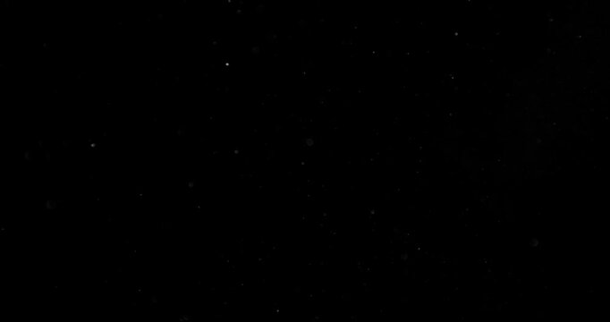 Super slow motion falling snow or dust particles isolated on a black background. Abstract atmospheric SFX overlay with floating debris, cinematic texture and dark visual effect.