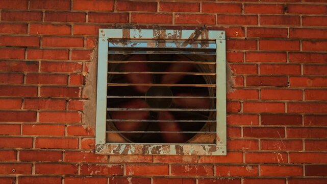 Industrial ventilation fan behind metal grid on red brick wall, urban infrastructure and ventilation system detail, 4K
