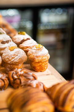 A minimalist, shallow depth of field shot showcasing rows of fresh icing-dusted cruffins and golden baked pastries displayed on a wooden counter in a cafe.