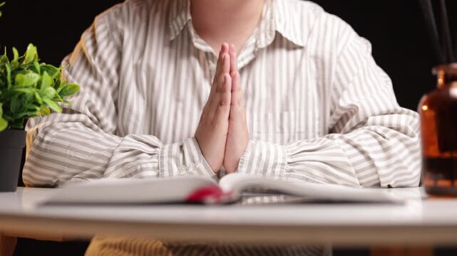 Person in striped shirt praying with hands together over open book