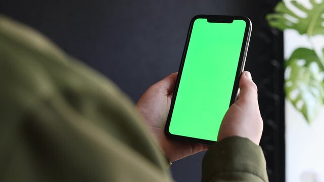 Person holding a smartphone with a green screen for content creation