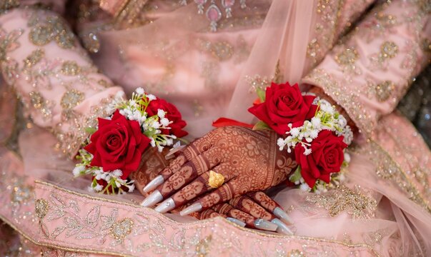 Closeup of bride hands with intricate henna mehndi, red rose gajra flower jewelry and gold ring
