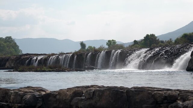 Static shot of Tad Hua Khon waterfall flowing through dense green forest on the Bolaven Plateau in southern Laos.