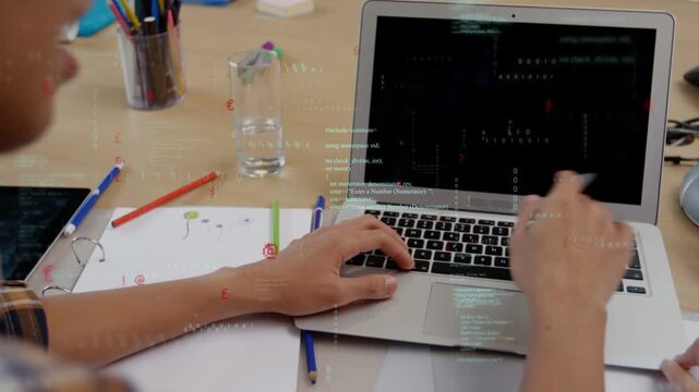 Male developer coding on laptop, tapping trackpad and pointing with pen, responding to colleague