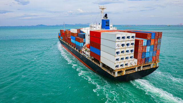 Cargo ships, carrying containers of goods, set sail at sea to deliver the goods to their destination.