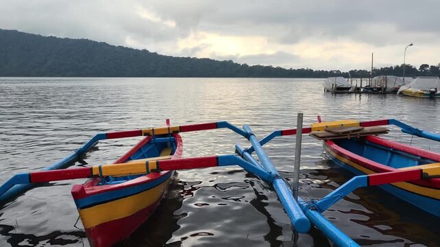Traditional colorful jukung outrigger boats moored on Lake Tamblingan under a cloudy sky in Bali