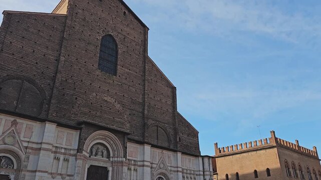 Street-level view of the brick facade of the Basilica of San Petronio in Bologna, Emilia-Romagna, Italy, under blue sky.