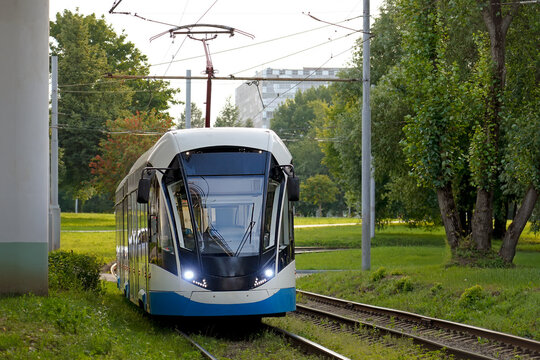 A passenger electric tram travels way turn junction in a green park, city transport