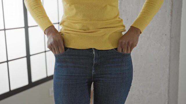Woman shows empty pockets with hands partly clenched and yellow sweater in a studio; financial struggle frustration.