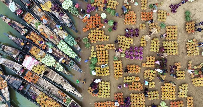 Aerial view of a vibrant floating market with wooden boats and piles of colorful vegetables and people working at the riverbank in Sylhet, Sylhet Division, Bangladesh.