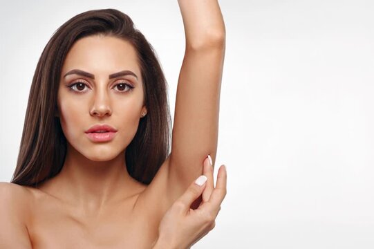 Young woman with long dark hair posing gracefully, highlighting her perfectly smooth underarm skin in a bright studio setting