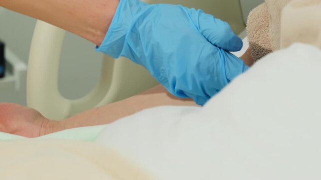 Blue gloved hands remove adhesive strip from IV catheter on woman arm. Medical worker peels cover away clearing dressing for line check