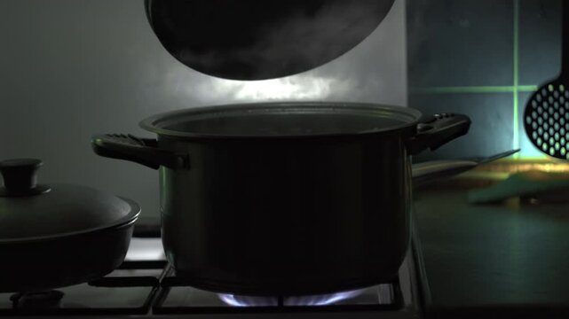 In kitchen on gas stove human hand lifts the lid from the pot, triggering a release of steam