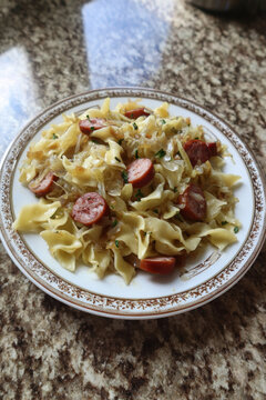 Delicious traditional polish haluski dish consisting of fried egg noodles mixed with sauteed green cabbage onions and sliced smoked kielbasa sausage served on a decorative white ceramic plate