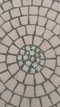 Top view circular paving stones park, close-up radial cobblestone pattern with moss lined joints, neutral beige and gray tones