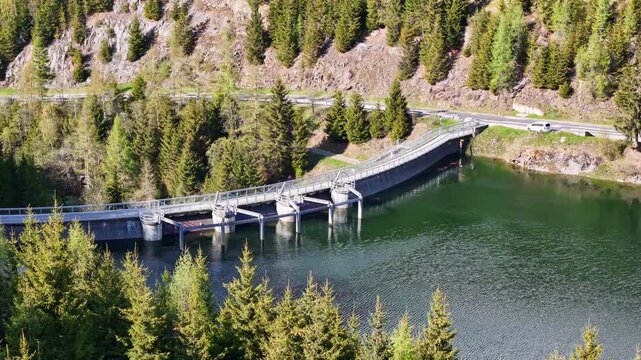 Aerial view of Kraftwerk Bodendorf and Sperre Paal dam surrounded by lush evergreen forests and a calm reservoir in Murau, Styria, Austria.