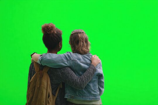 Two women, back view, embracing, looking up, against green screen