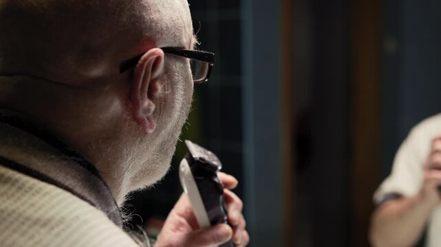 Pension man shaves his mustache with a trimmer in front of a bathroom mirror