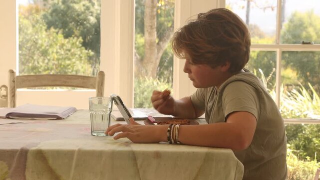 12 year old boy eating lunch and using smart phone at home
