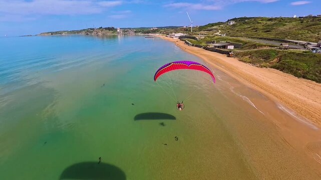 Aerial view of a paramotor flying over the sandy Kilyos beach and turquoise waters in Kumkoy, Istanbul, Turkey.