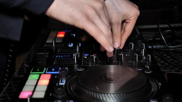 DJ mixes dance rhythm on mixing console. DJ playing music at a party in a nightclub.DJ hands touching buttons and sliders while playing electronic music.DJ console