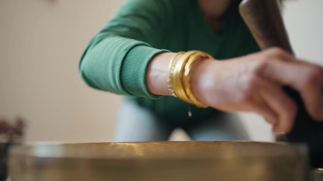 Hand circles a mallet around a Tibetan singing bowl seen from a low angle