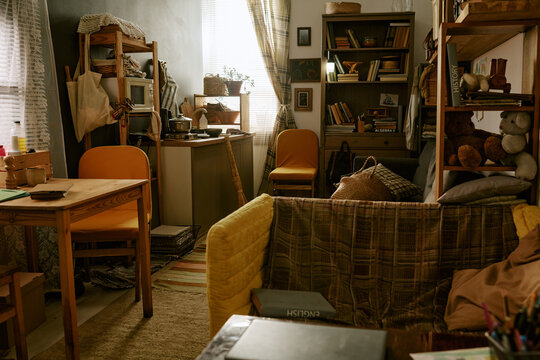 Wide shot of cramped studio apartment showing compact kitchen, desk, sofa, storage shelves, conveying poverty and small space living. Useful for housing crisis, low income lifestyle marketing
