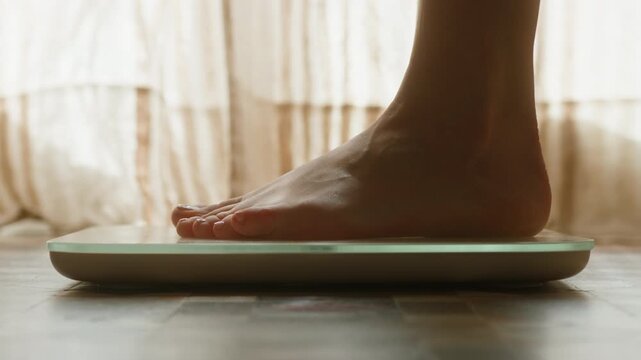 Close-up of feet stepping onto a digital bathroom scale for weighing. Concept of weight control, health monitoring, fitness goals, body care, and healthy lifestyle at home. High quality 4k footage