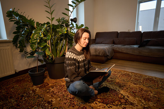 Woman reading a book while sitting on a patterned rug in a cozy living room