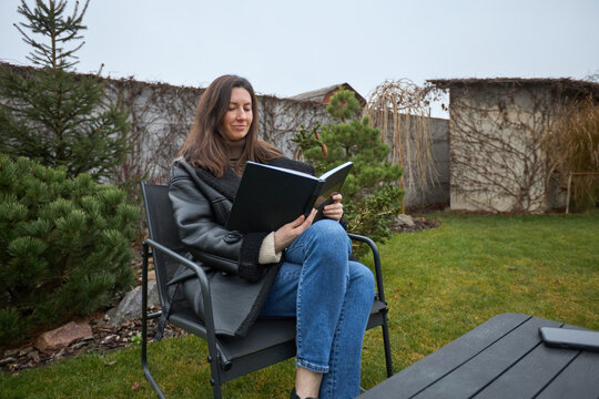 Woman in a cozy jacket reading a book outdoors on a cool day