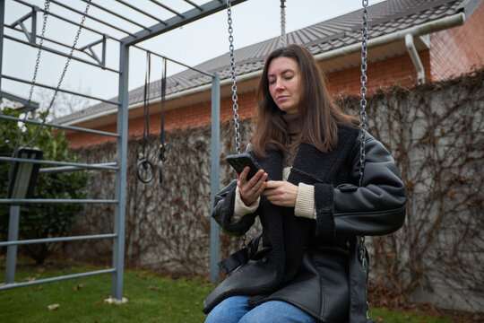 Woman on swing checking her phone in a backyard with outdoor gym equipment