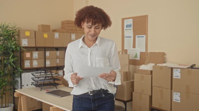 Woman holds paper with both hands reads it and raises fist in office building; small business success joy.