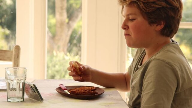 12 year old boy eating lunch and using smart phone at home