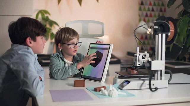 While 3D printer working, two boys discuss and research printed part