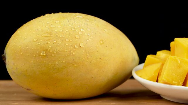 Close-up pan from a fresh ripe yellow mango with water drops to a plate of diced mango.
