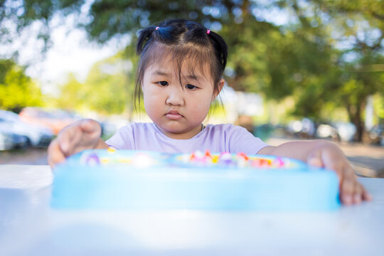Cute little Asian girl concentrating intently while playing a fishing board game outdoors,A concentrated and focused little Asian girl playing a plastic magnetic fishing toy game on a table.