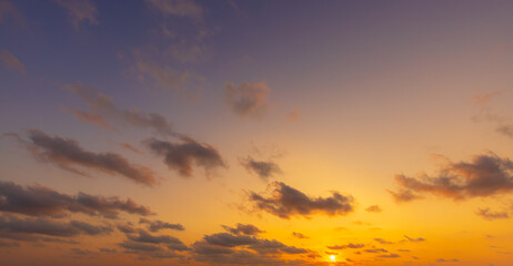 Obraz premium Majestic Sunset with Scattered Clouds,A breathtaking view of the golden hour sky during sunset, featuring vibrant orange and yellow hues blending into a soft purple gradient with scattered, wispy.