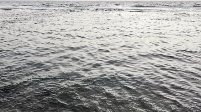 Calm ocean water surface with small waves moving towards a flat horizon