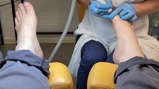 Close-up male foot receiving hardware pedicure, master technician uses diamond cutter and gloved hands to remove callus and shape