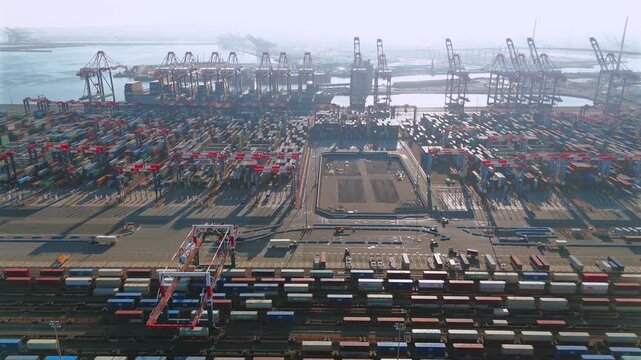 Aerial tracking footage of container terminal with cranes and freight trains