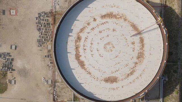 Aerial view of a large circular industrial storage tank with concentric patterns on its roof and surrounding infrastructure in Priolo Gargallo, Sicily, Italy.