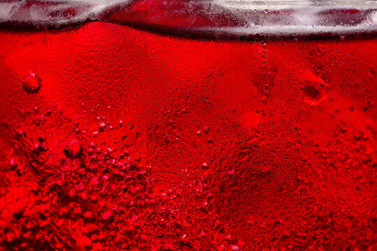 Macro shot of cold red drink with condensation droplets on glass,Close-up macro texture of a refreshing cold red beverage in a glass, covered with condensation water droplets and small ice bubbles.