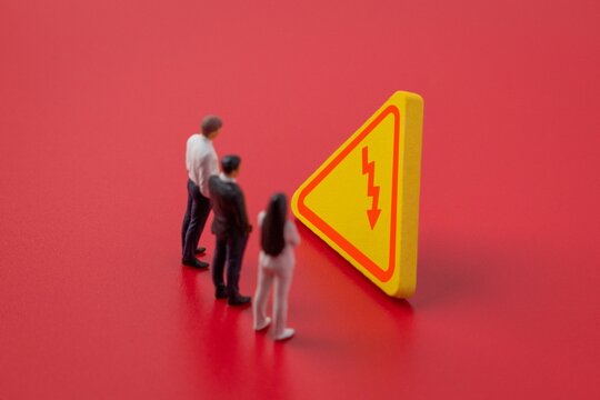 Three miniature business figures facing a sign with a downward red arrow on a red background. Economic downturn, business risk, financial crisis, corporate failure, and market decline concept.